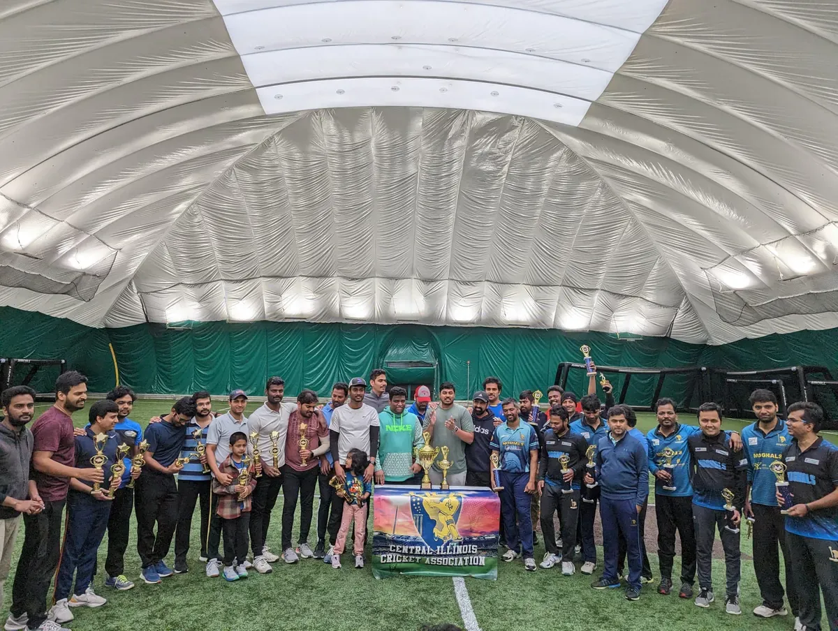 A large group gathered around a trophy table inside an indoor cricket facility.