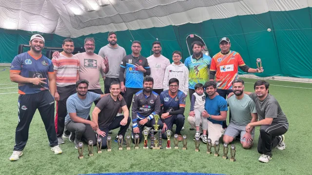 A group of cricketers gathered with trophies on an indoor field.