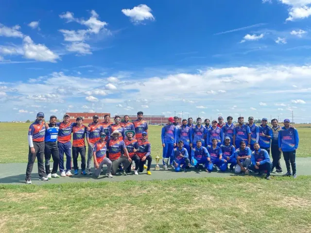 Cricket teams standing together on an outdoor field beneath a blue sky.